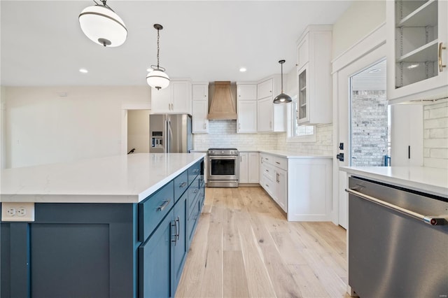 kitchen with stainless steel appliances, custom exhaust hood, blue cabinets, and white cabinets