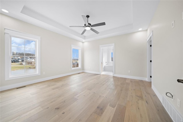 empty room with light hardwood / wood-style floors, a raised ceiling, and ceiling fan