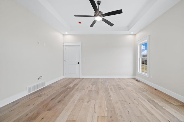 spare room with a raised ceiling, ceiling fan, and light wood-type flooring