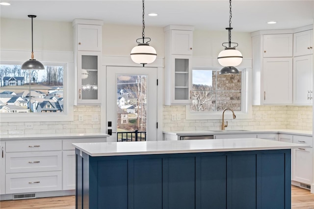 kitchen with light countertops, visible vents, white cabinetry, a kitchen island, and a sink