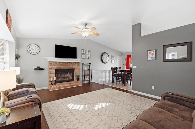 living room with dark wood-type flooring, ceiling fan, vaulted ceiling, and a brick fireplace