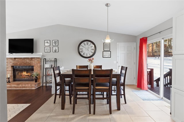 tiled dining space with lofted ceiling and a brick fireplace