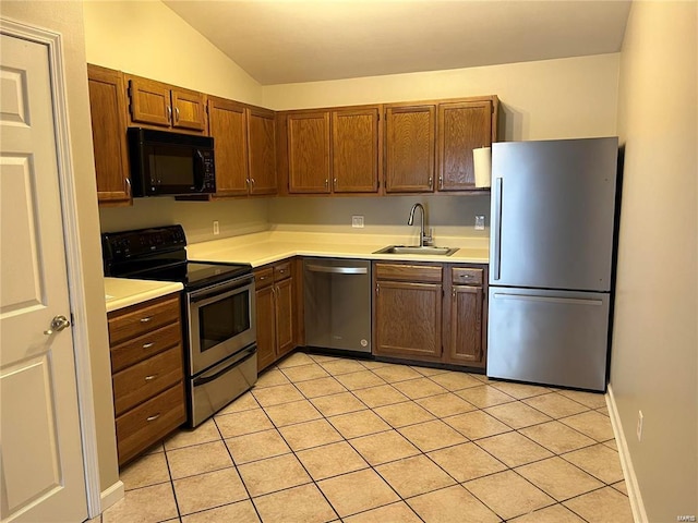 kitchen with vaulted ceiling, appliances with stainless steel finishes, sink, and light tile patterned floors