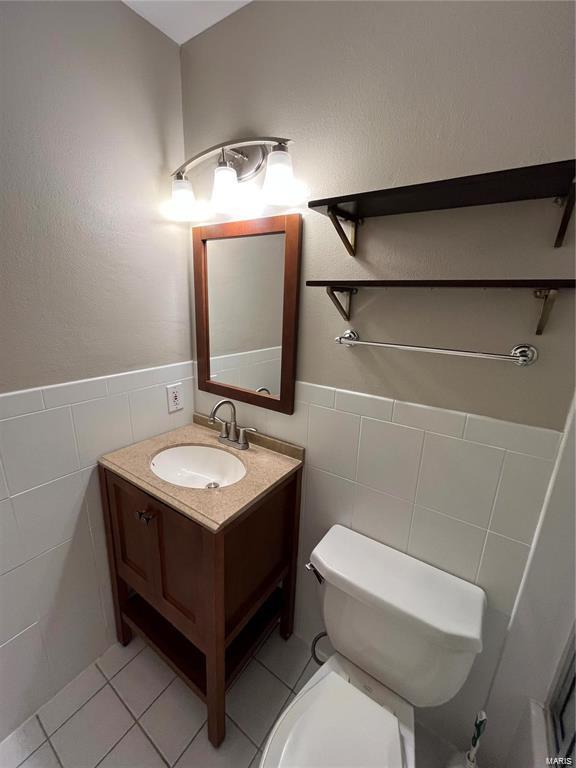 bathroom featuring tile patterned floors, vanity, toilet, and tile walls