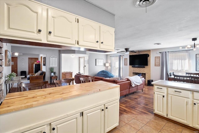 kitchen featuring ceiling fan with notable chandelier, a brick fireplace, and light tile patterned floors