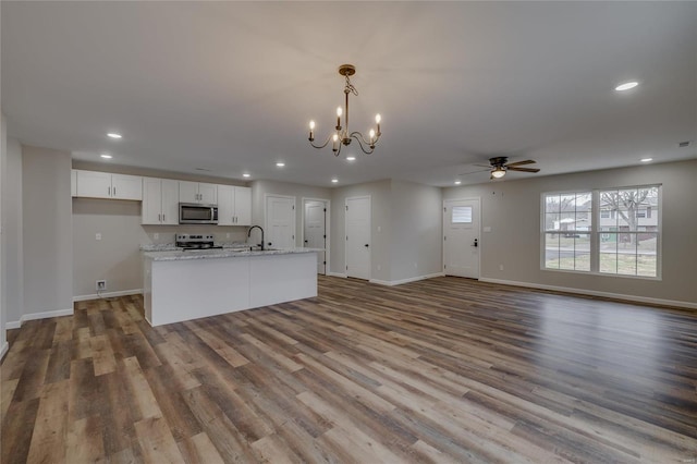 kitchen featuring decorative light fixtures, white cabinetry, light stone counters, stainless steel appliances, and a center island with sink