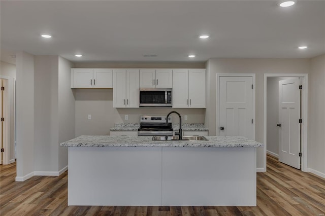 kitchen with appliances with stainless steel finishes, white cabinetry, sink, a kitchen island with sink, and light stone countertops