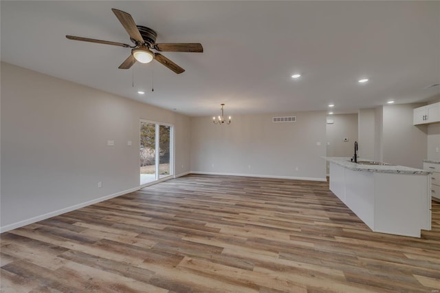 unfurnished living room featuring ceiling fan with notable chandelier, sink, and light hardwood / wood-style flooring