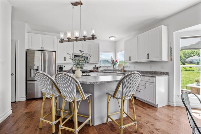 kitchen with stainless steel refrigerator with ice dispenser, white cabinetry, a kitchen island, and hanging light fixtures