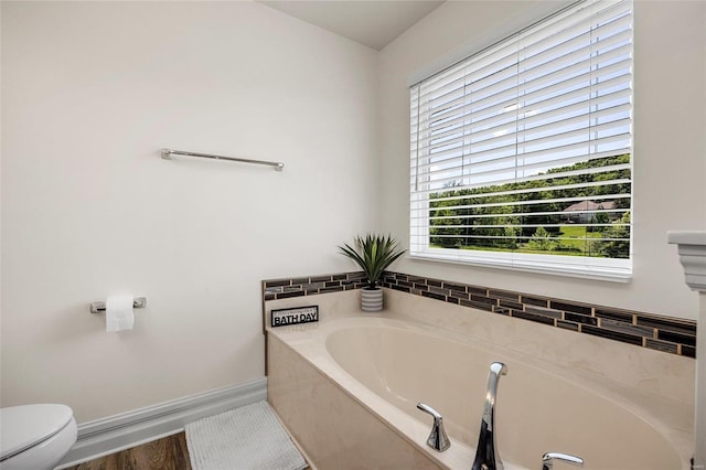 bathroom with a tub to relax in and toilet