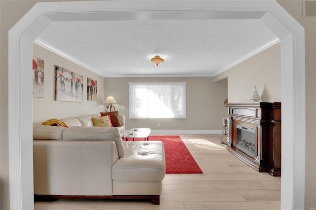 living room with light wood-type flooring, a textured ceiling, crown molding, and a glass covered fireplace