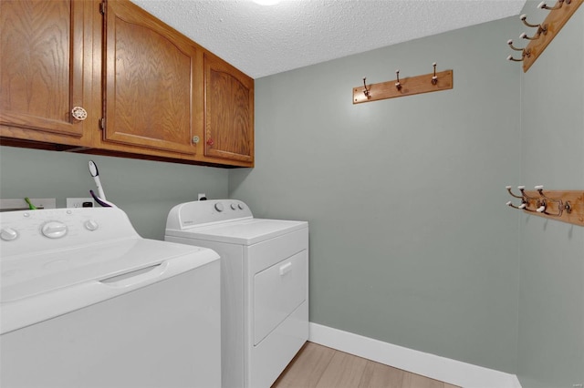 laundry area with a textured ceiling, separate washer and dryer, baseboards, cabinet space, and light wood finished floors