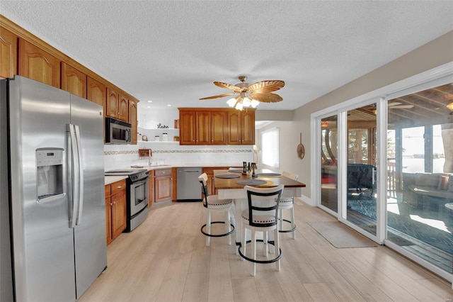 kitchen featuring appliances with stainless steel finishes, brown cabinetry, light wood-type flooring, and decorative backsplash