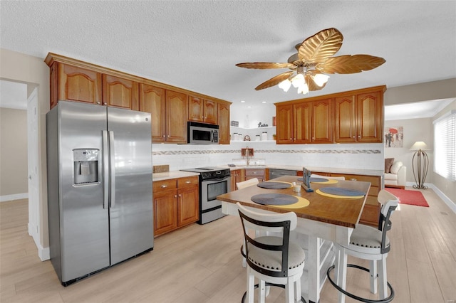 kitchen with appliances with stainless steel finishes, brown cabinetry, light wood-style floors, and backsplash