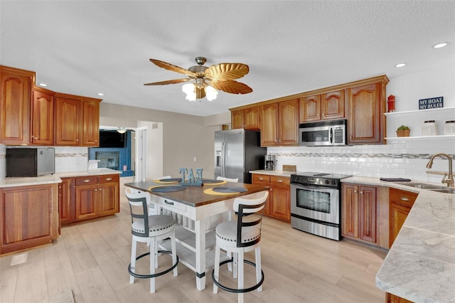 kitchen featuring brown cabinets, stainless steel appliances, light countertops, a sink, and ceiling fan