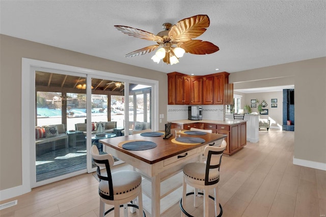 kitchen featuring visible vents, light countertops, light wood-style flooring, brown cabinetry, and a peninsula