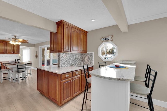 kitchen featuring a peninsula, a breakfast bar area, brown cabinets, and beam ceiling