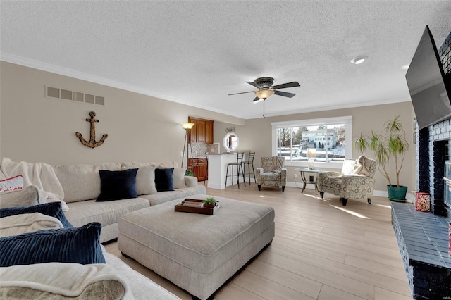 living area featuring light wood-style floors, visible vents, a fireplace, and crown molding