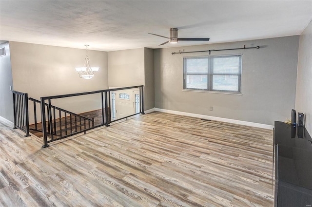 spare room featuring ceiling fan with notable chandelier and light hardwood / wood-style floors