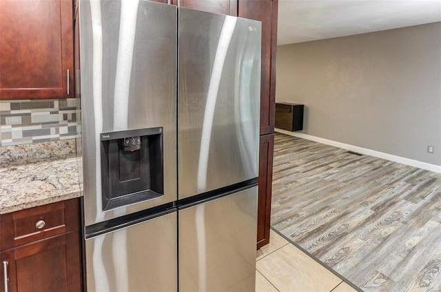 kitchen with tasteful backsplash, light stone countertops, light hardwood / wood-style floors, and stainless steel refrigerator with ice dispenser