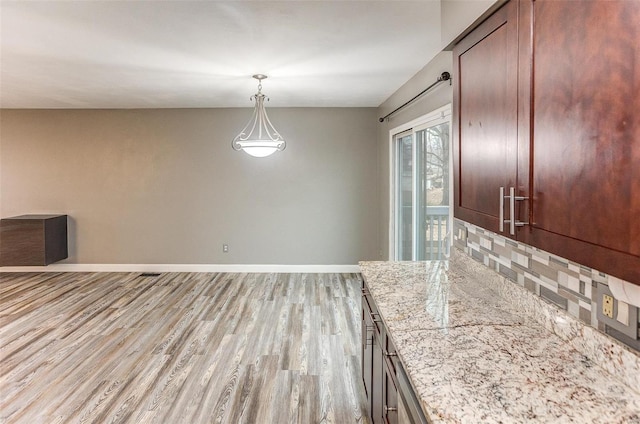 kitchen with hanging light fixtures, light stone countertops, backsplash, and light hardwood / wood-style flooring