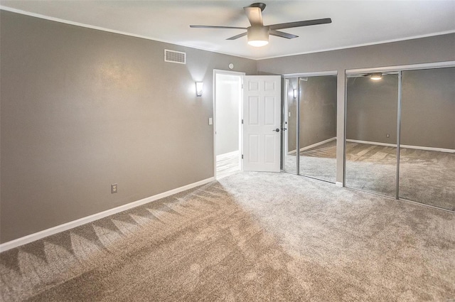 unfurnished bedroom with crown molding, two closets, ceiling fan, and carpet flooring