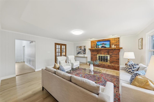 living room with french doors, ornamental molding, a brick fireplace, and light hardwood / wood-style flooring