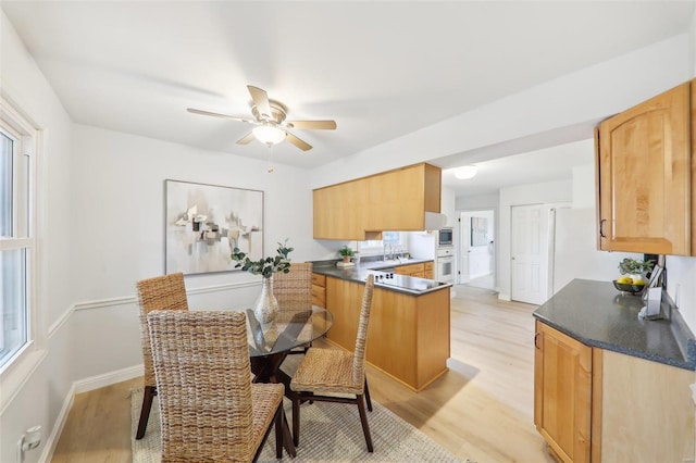 kitchen featuring stainless steel microwave, kitchen peninsula, oven, ceiling fan, and light hardwood / wood-style floors