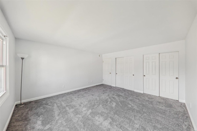 unfurnished bedroom featuring dark carpet and multiple closets