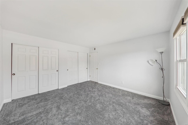 unfurnished bedroom featuring dark carpet and two closets