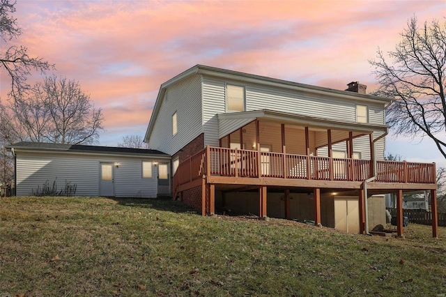 back house at dusk featuring a wooden deck and a yard