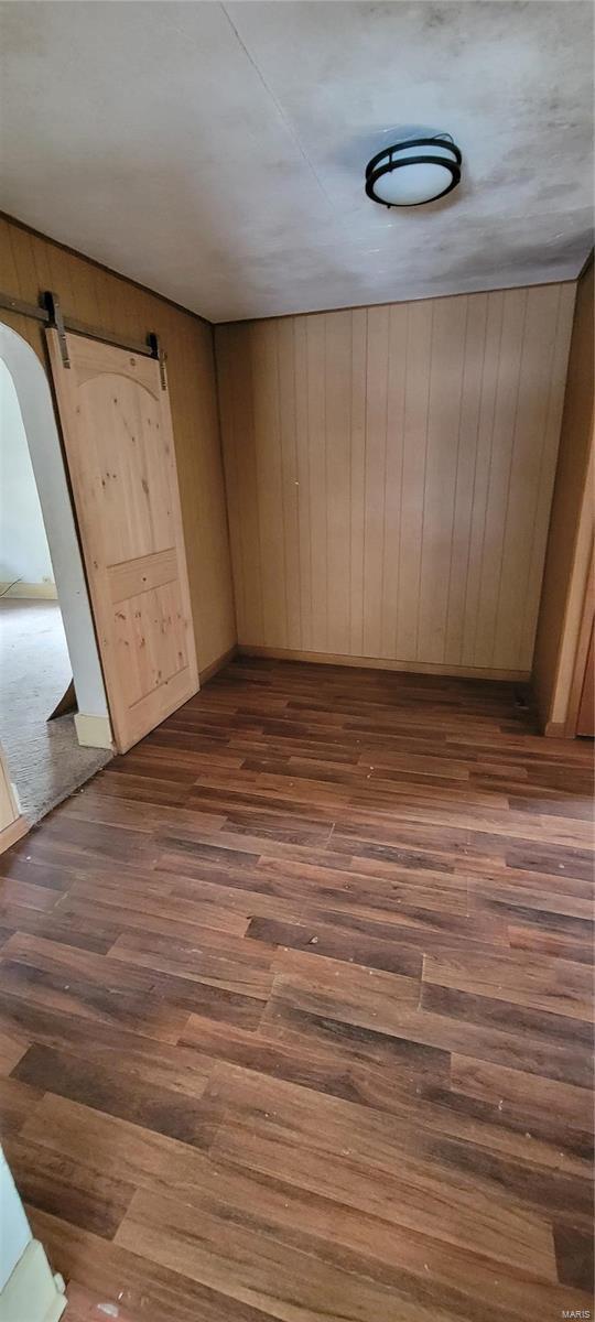 empty room with dark hardwood / wood-style floors, a barn door, and wood walls