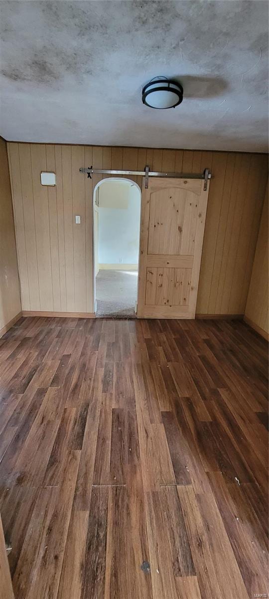 empty room featuring a barn door, dark wood-type flooring, a textured ceiling, and wood walls