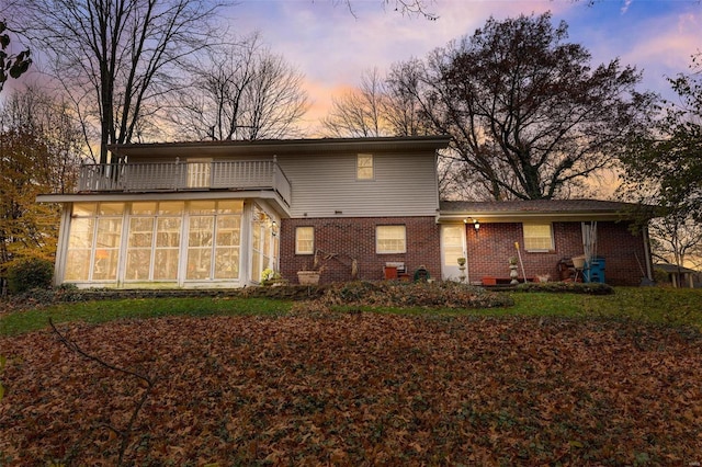 back house at dusk featuring a balcony and a sunroom