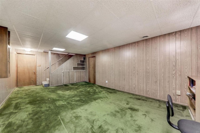 basement featuring a drop ceiling, carpet floors, and wood walls