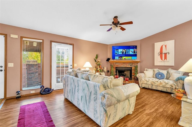 living room with ceiling fan, a fireplace, vaulted ceiling, and light wood-type flooring