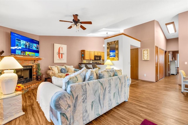 living room with lofted ceiling, a fireplace, ceiling fan, and light wood-type flooring