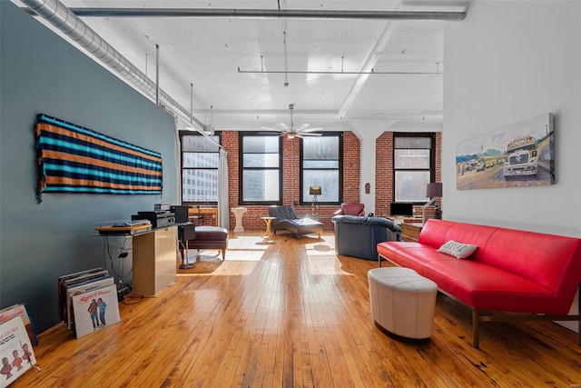 living room featuring hardwood / wood-style flooring, ceiling fan, and brick wall