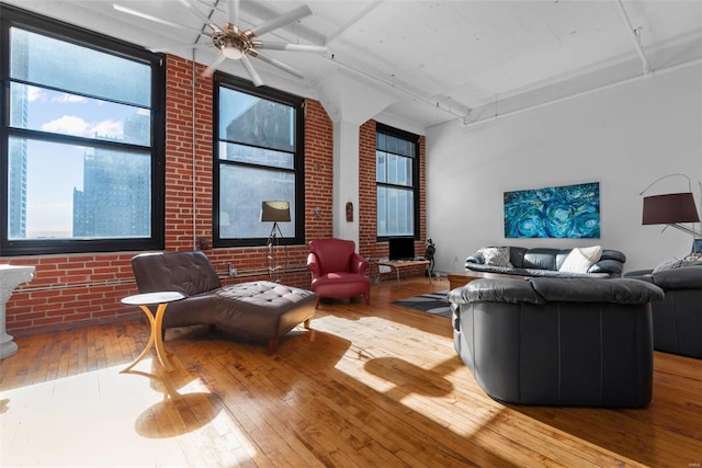 living room with ceiling fan, a towering ceiling, brick wall, and light wood-type flooring