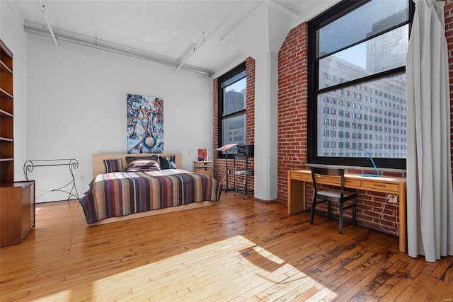 bedroom featuring wood-type flooring and brick wall