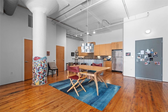 dining area with rail lighting, a towering ceiling, and hardwood / wood-style floors