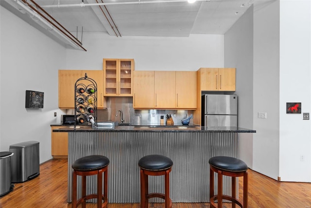 kitchen with stainless steel fridge, a breakfast bar area, light hardwood / wood-style floors, kitchen peninsula, and light brown cabinets