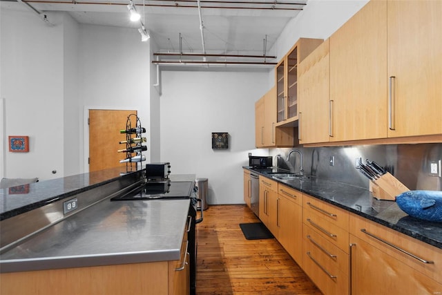 kitchen with light brown cabinetry, sink, stainless steel counters, stainless steel dishwasher, and light hardwood / wood-style floors