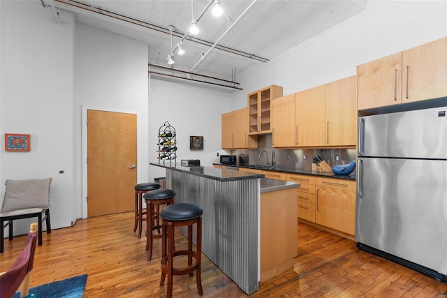 kitchen featuring a breakfast bar area, stainless steel refrigerator, a high ceiling, and light brown cabinets