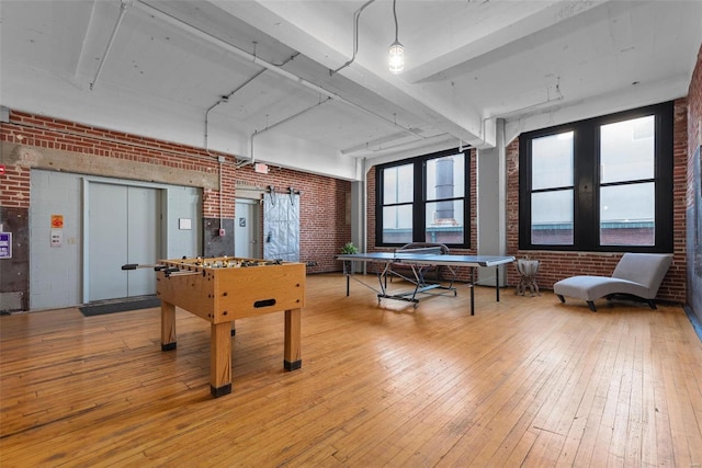 recreation room featuring brick wall and light wood-type flooring