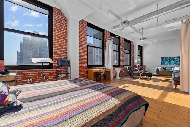 bedroom featuring multiple windows, hardwood / wood-style floors, a towering ceiling, and brick wall