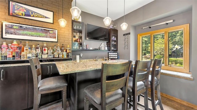 bar featuring light stone counters, dark brown cabinetry, and decorative light fixtures