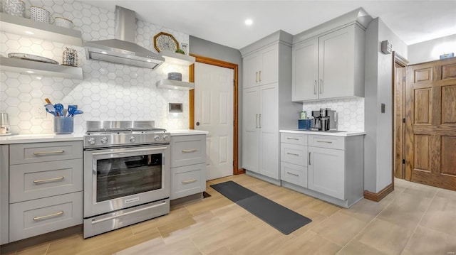 kitchen featuring wall chimney exhaust hood, stainless steel stove, decorative backsplash, and gray cabinetry