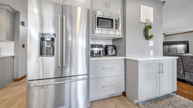 kitchen featuring appliances with stainless steel finishes, gray cabinetry, decorative backsplash, light hardwood / wood-style floors, and kitchen peninsula