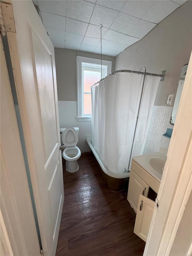 full bathroom with shower / tub combo with curtain, hardwood / wood-style flooring, vanity, a drop ceiling, and toilet